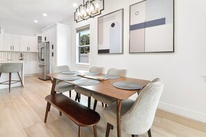 A modern dining area with a wooden table, grey upholstered chairs, and a bench. - Walk to Raymond James Stadium 3 Bedroom West Tampa Midtown Luxury Home (Tampa)