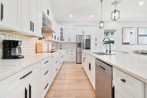 A modern kitchen with white cabinetry, stainless steel appliances, and a central island with a sink. - Walk to Raymond James Stadium 3 Bedroom West Tampa Midtown Luxury Home (Tampa)