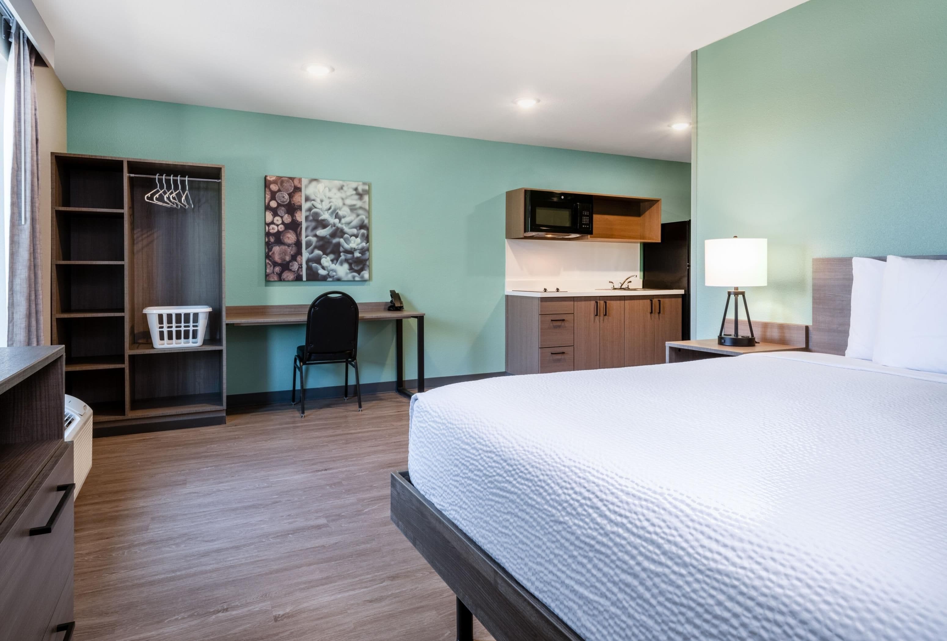 Une chambre d’hôtel équipée d’un lit, d’un bureau, d’une chaise, d’une armoire, d’un four à micro-ondes et d’une lampe.