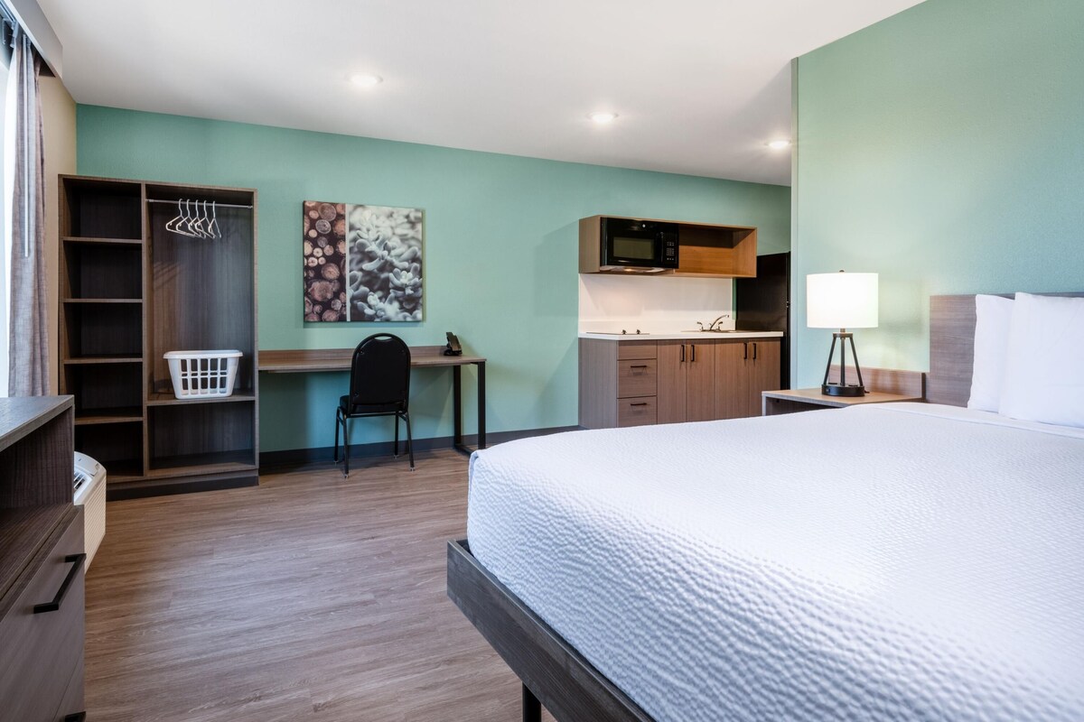 Habitación de hotel con cama, escritorio, silla, armario, microondas y lámpara.