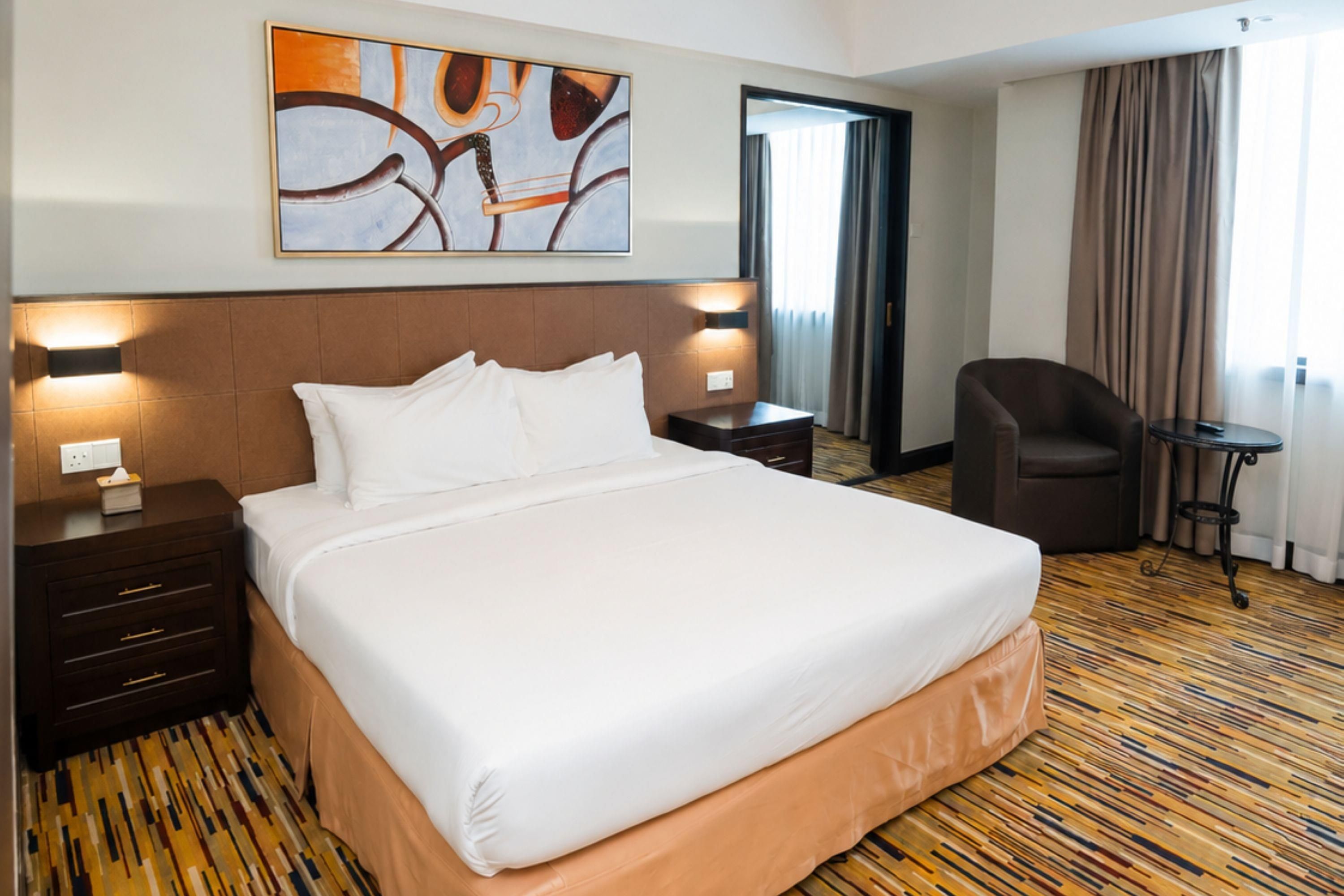 A hotel room with a large bed, a desk, a chair, and a painting on the wall.