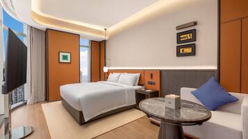 Une chambre d’hôtel avec un lit, un canapé, une petite table, une télévision et une fenêtre avec des rideaux.
