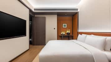 Une chambre d’hôtel avec un grand lit, un téléviseur à écran plat, une porte en bois et une petite table agrémentée de fleurs.