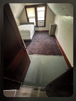 Une chambre à coucher avec un lit, une table de chevet, une fenêtre et un sol recouvert d’une moquette.