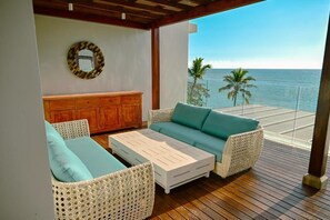 Ein Balkon mit Korbmöbeln, einem Holzschrank und Blick aufs Meer.