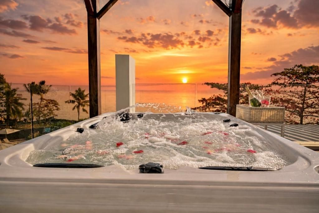 Un bain à remous avec vue sur le coucher de soleil, entouré de palmiers et d’une structure en bois.