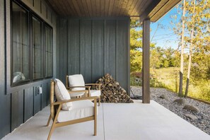 A covered outdoor seating area with a chair and a stack of firewood. - Firefly Landing | Pet Friendly | Golf (Elk Rapids)