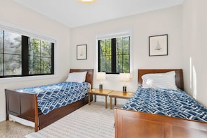 A bedroom with two beds, a small table, and framed pictures on the wall. - Firefly Landing | Pet Friendly | Golf (Elk Rapids)