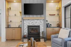 A living room with a fireplace, a television mounted above it, and a sofa. - Firefly Landing | Pet Friendly | Golf (Elk Rapids)