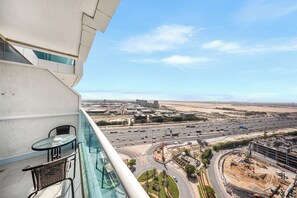 A balcony with a glass table and chairs, overlooking a busy highway and construction site. - StayShort - Studio with best skyline view in JVT for 2! (JVT)