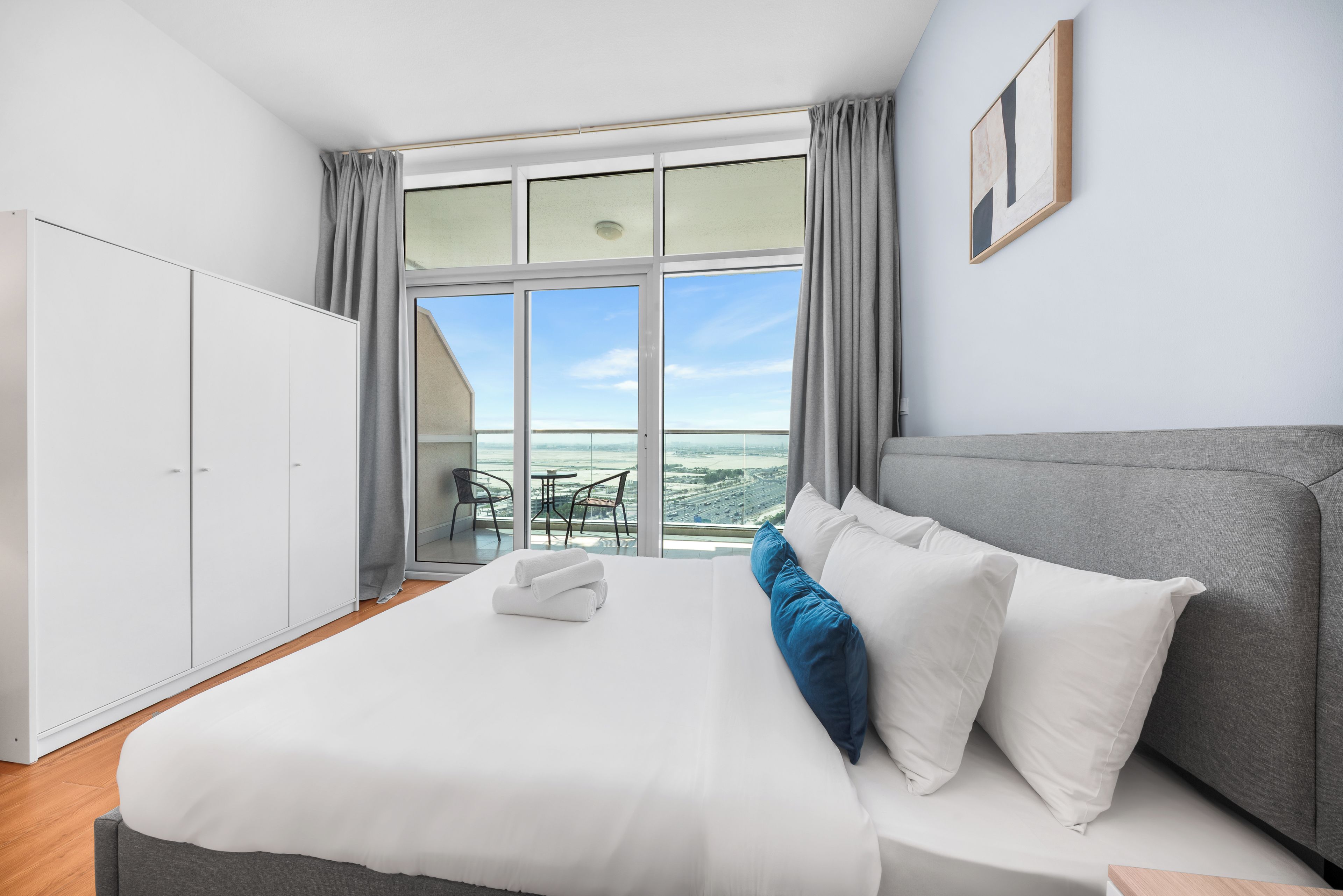 A hotel room with a bed, a wardrobe, a view of the cityscape, and a dining area with a table and chairs.