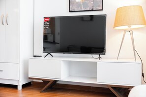 A flat-screen TV on a white entertainment unit with a lamp beside it. - StayShort - Studio with best skyline view in JVT for 2! (JVT)