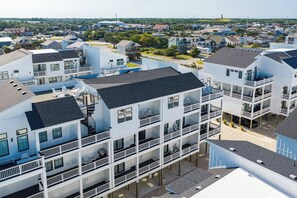 A multi-story residential building with balconies, a covered outdoor area, and a view of the surrounding neighborhood. - Brand New Condo w/ Ocean Views, Elevator, Pool! (Kill Devil Hills)