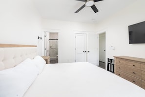 A bedroom with a bed, a wooden dresser, a ceiling fan, and a TV mounted on the wall. - Brand New Condo w/ Ocean Views, Elevator, Pool! (Kill Devil Hills)