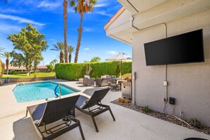 A swimming pool with lounge chairs, a grill, and a flat-screen TV mounted on a wall. - Private Pool & Firepit Escape in Mission Hills Country Club | Mountain Views, Golf & Pickleball (Rancho Mirage)