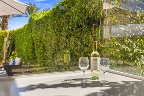 A table with two wine glasses and a bottle of wine, set against a backdrop of lush greenery. - Private Pool & Firepit Escape in Mission Hills Country Club | Mountain Views, Golf & Pickleball (Rancho Mirage)