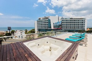 Ein Poolbereich auf dem Dach mit Whirlpool, Liegestühlen und Blick auf das Meer und die Hotelgebäude.
