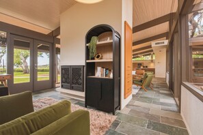 Ein modernes Interieur mit Kamin, grünen Polstersesseln und Blick ins Freie durch große Glasüren.