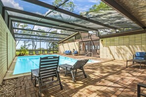 A covered outdoor swimming pool with lounge chairs and a patio area. - Spacious 4 BR GULF Front POOL Home! Private Dock with Boat Lift! FREE Golf Cart! (Palm Harbor)