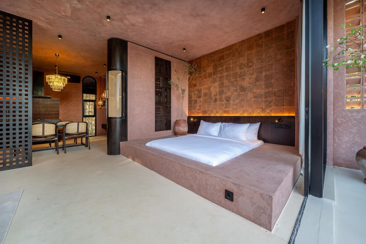 Quarto moderno com cama grande, área de jantar e parede decorativa.