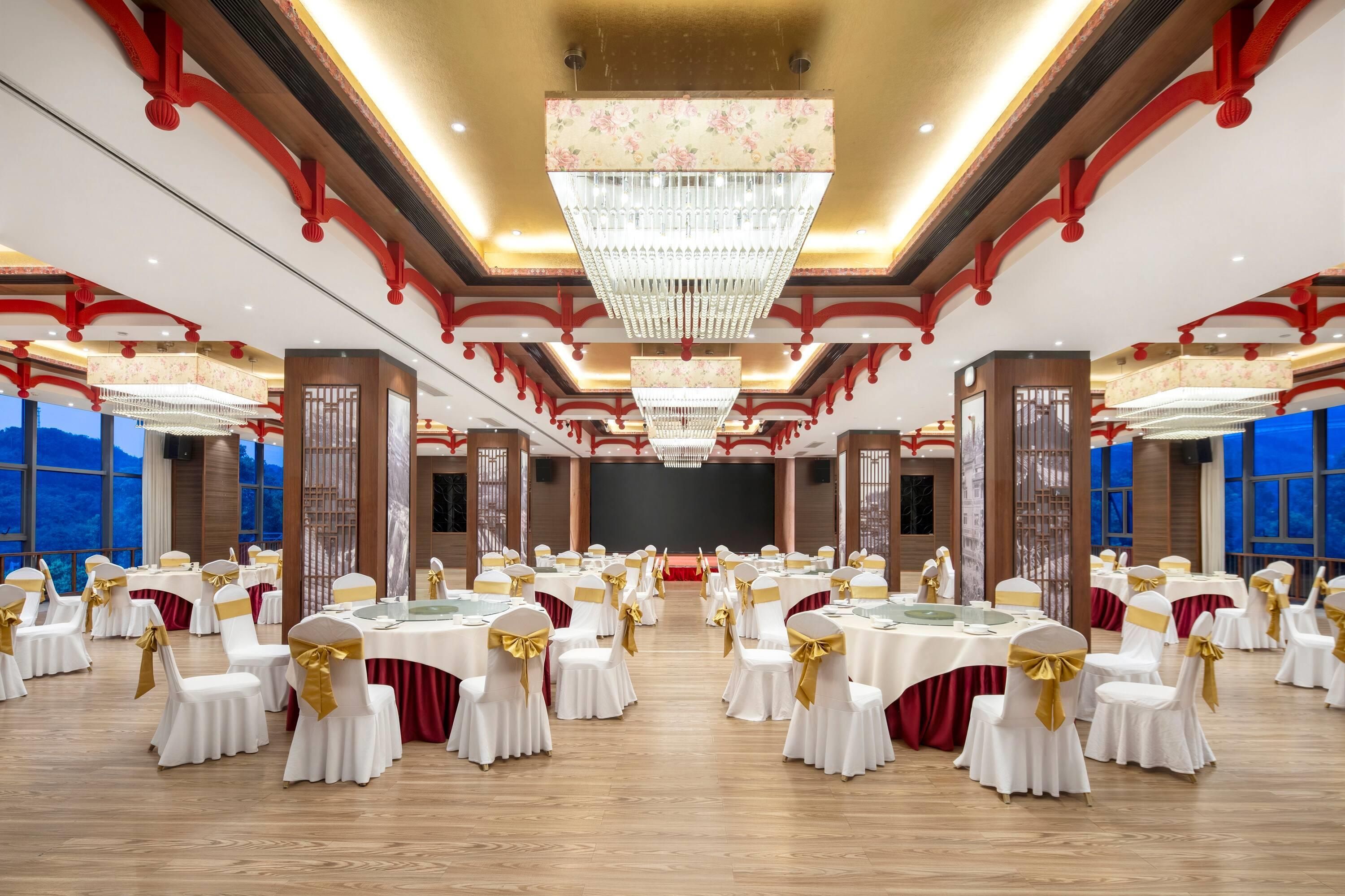 Una sala da banchetto con tavoli rotondi, sedie bianche con nastri dorati e un grande lampadario.
