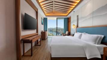 Habitación de hotel con una cama grande, televisión de pantalla plana, banca de madera, escritorio y vista al exterior.
