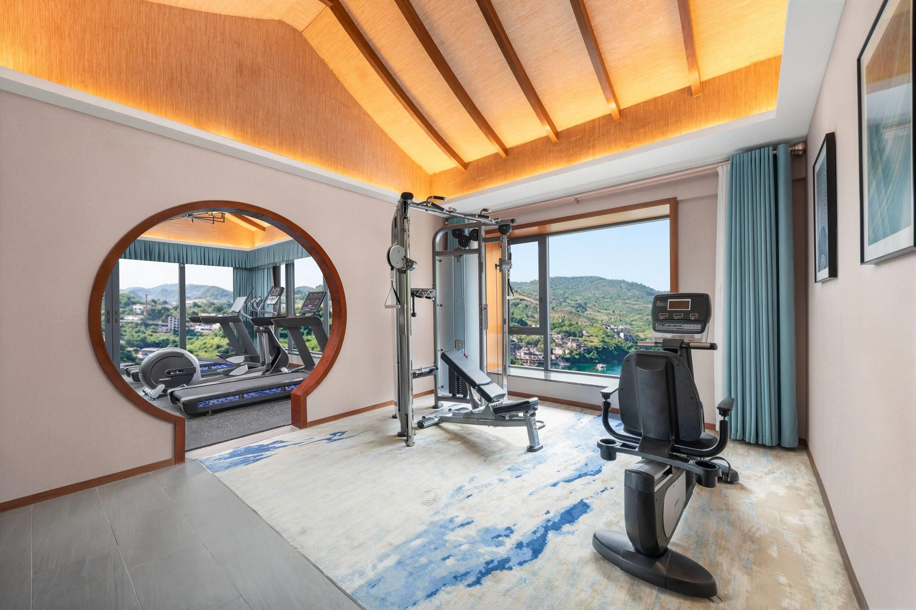 A gym with exercise equipment, a large mirror, and a view of the outdoors.