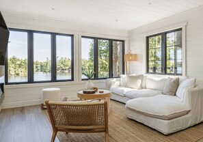 A room with a white sofa, a wicker chair, and a round wooden table with a vase and a candle. - Darling 4 bed 2 bath cottage on Lake Muskoka, minutes from Bala (Parry Sound Mid-Shore (Bala))