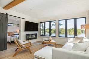 A modern living room with a fireplace, a sofa, a chair, and a television. - Darling 4 bed 2 bath cottage on Lake Muskoka, minutes from Bala (Parry Sound Mid-Shore (Bala))