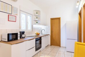 Una cocina compacta con armarios blancos, microondas, cafetera, lavamanos y refrigerador.