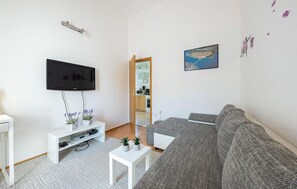 Ein modernes Wohnzimmer mit Flachbildfernseher, einem grauen Sofa, einem weißen Couchtisch und einem kleinen weißen Beistelltisch.