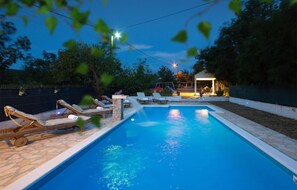Una piscina al aire libre con sillas de descanso y una zona techada.
