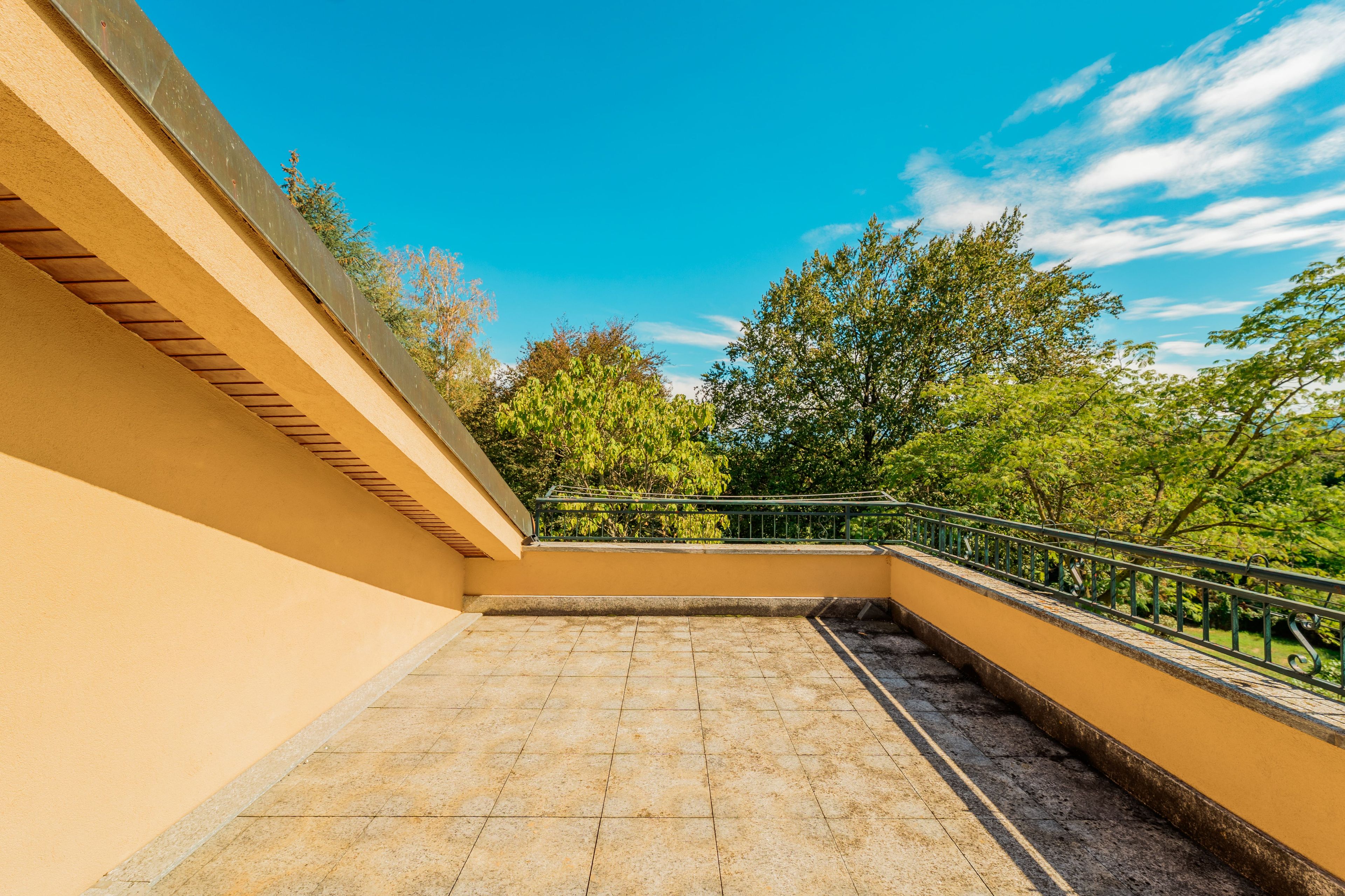 A balcony with a tiled floor, a metal railing, and a view of trees and sky.