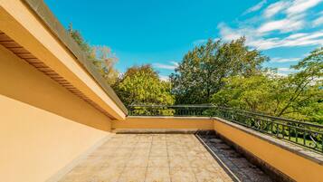 A balcony with a tiled floor, a metal railing, and a view of trees and sky.