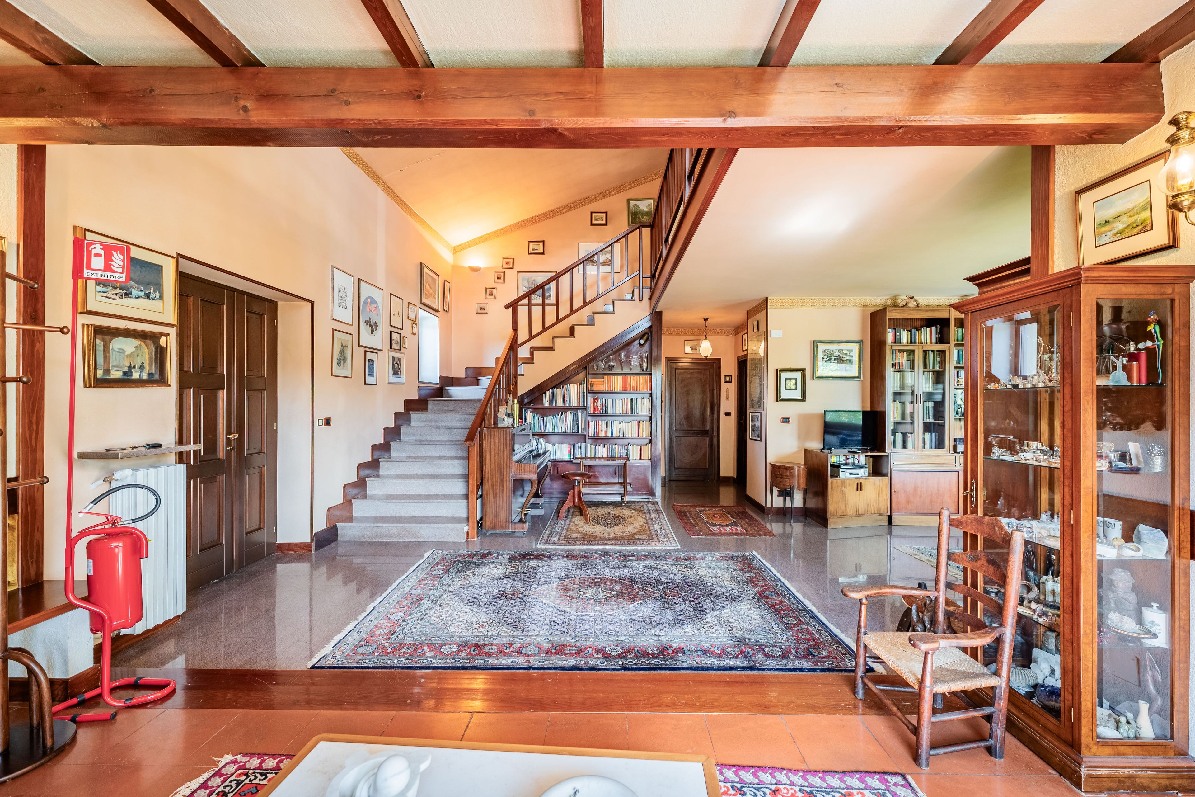A spacious living area with a wooden staircase, a fireplace, and a bookshelf.