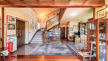A spacious living area with a wooden staircase, a fireplace, and a bookshelf.