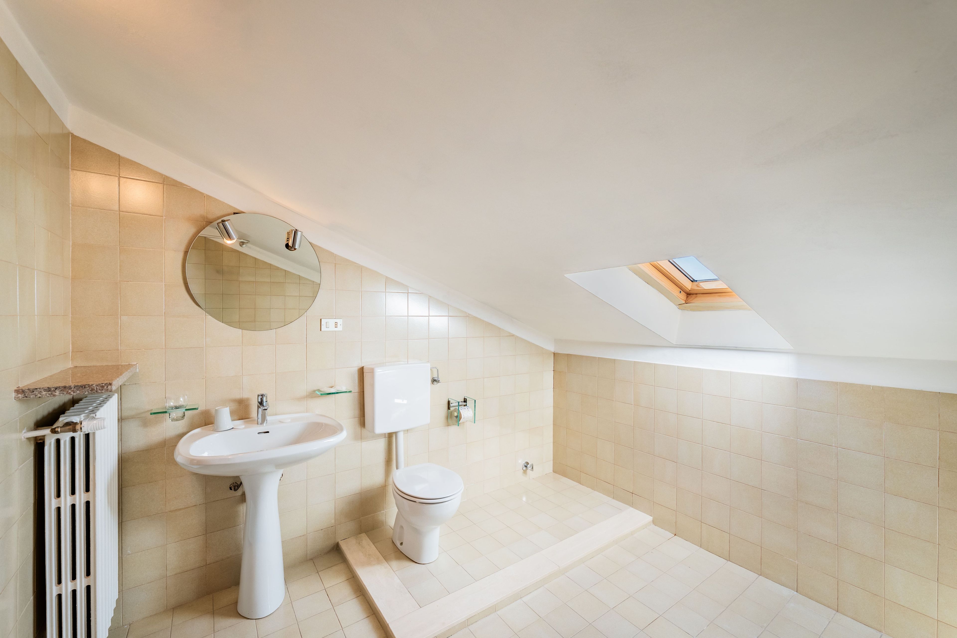 A modern bathroom with a skylight, a pedestal sink, a toilet, and a radiator.