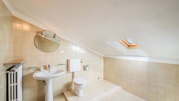 A modern bathroom with a skylight, a pedestal sink, a toilet, and a radiator.