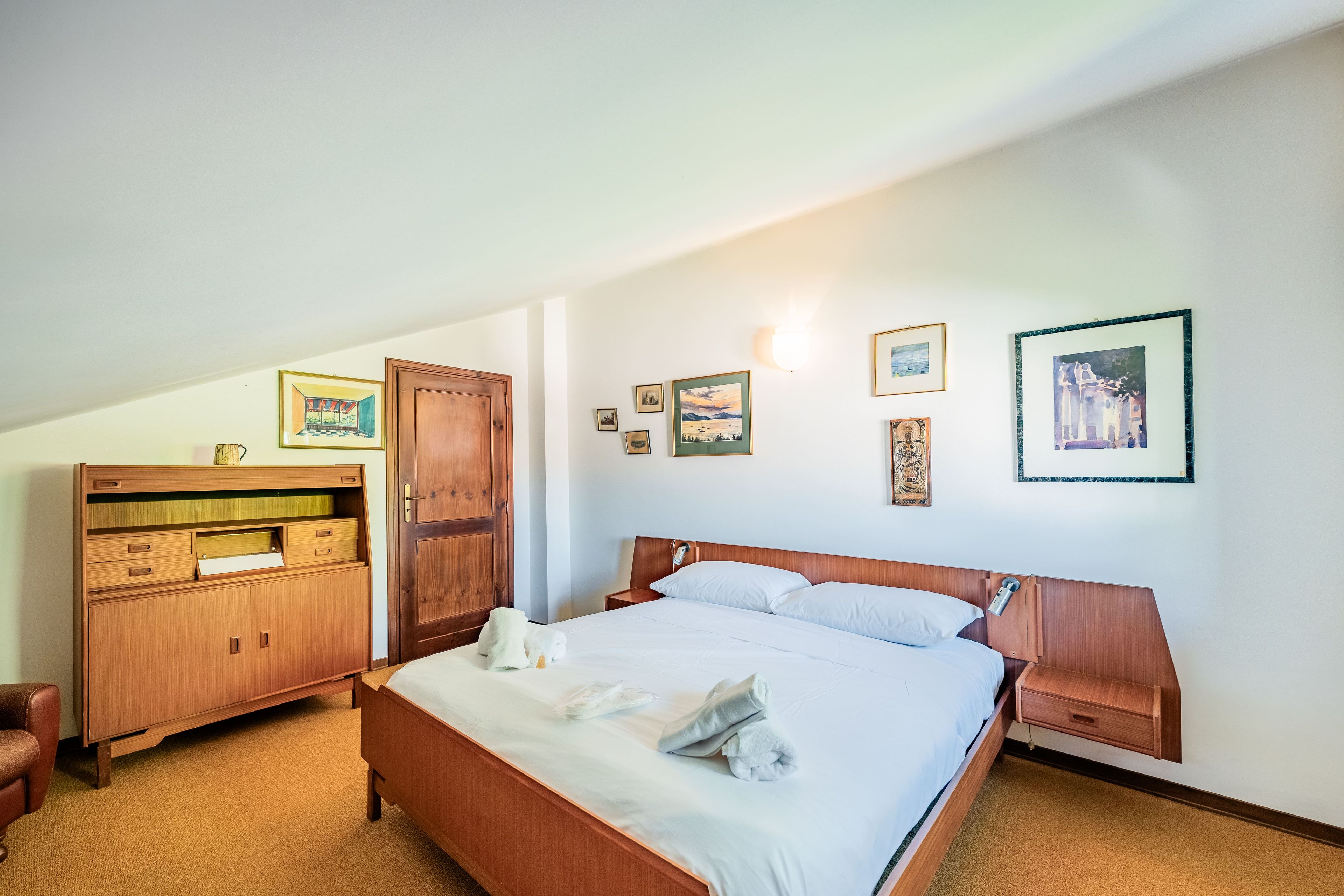 A hotel room with a bed, wooden wardrobe, and a desk.