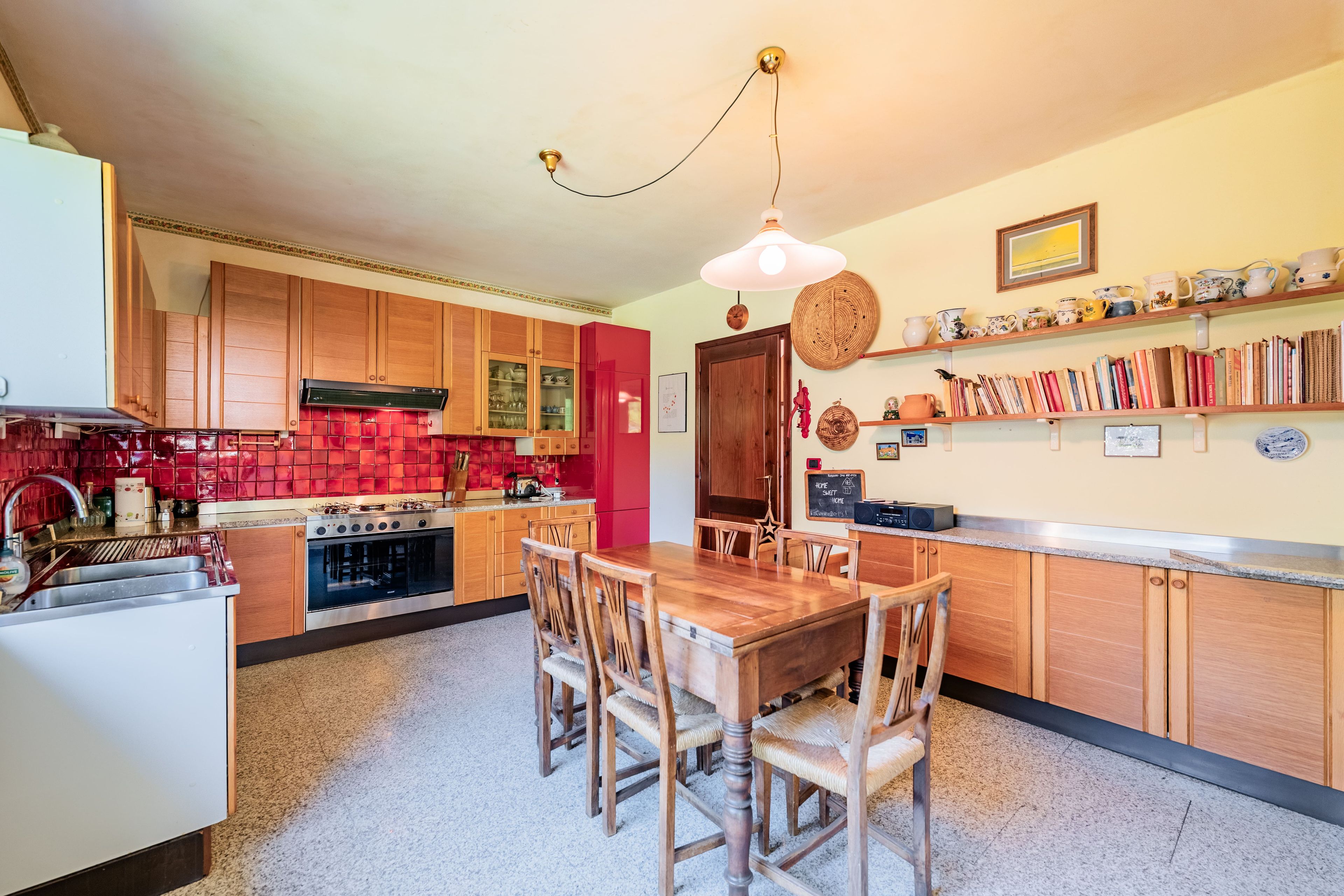A kitchen with wooden cabinets, a red backsplash, a dining table with chairs, and a hanging light fixture.