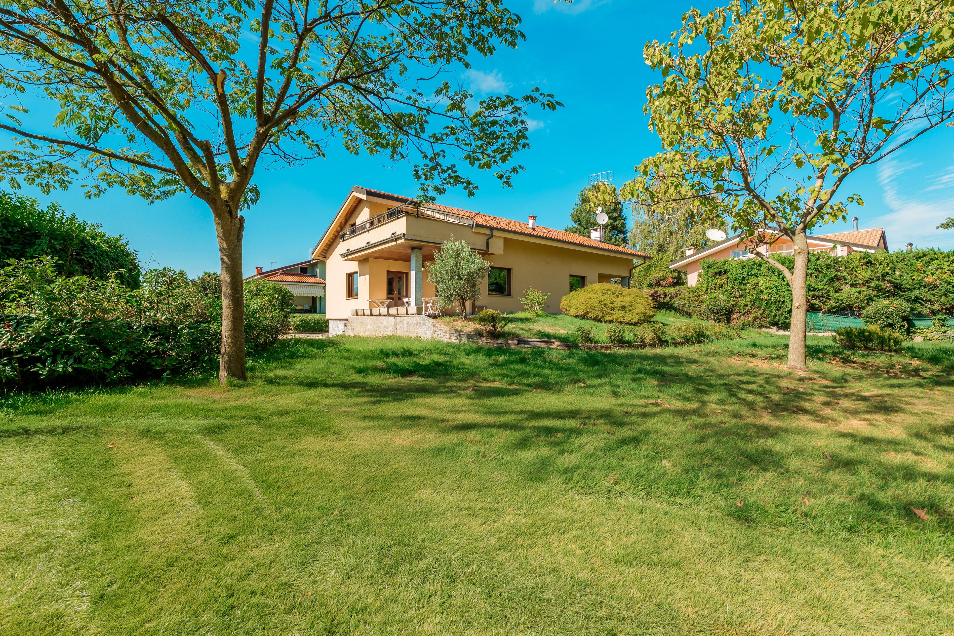 Une maison à deux étages dotée d’un balcon, entourée d’une pelouse bien entretenue et d’arbres.