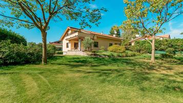 Une maison à deux étages dotée d’un balcon, entourée d’une pelouse bien entretenue et d’arbres.