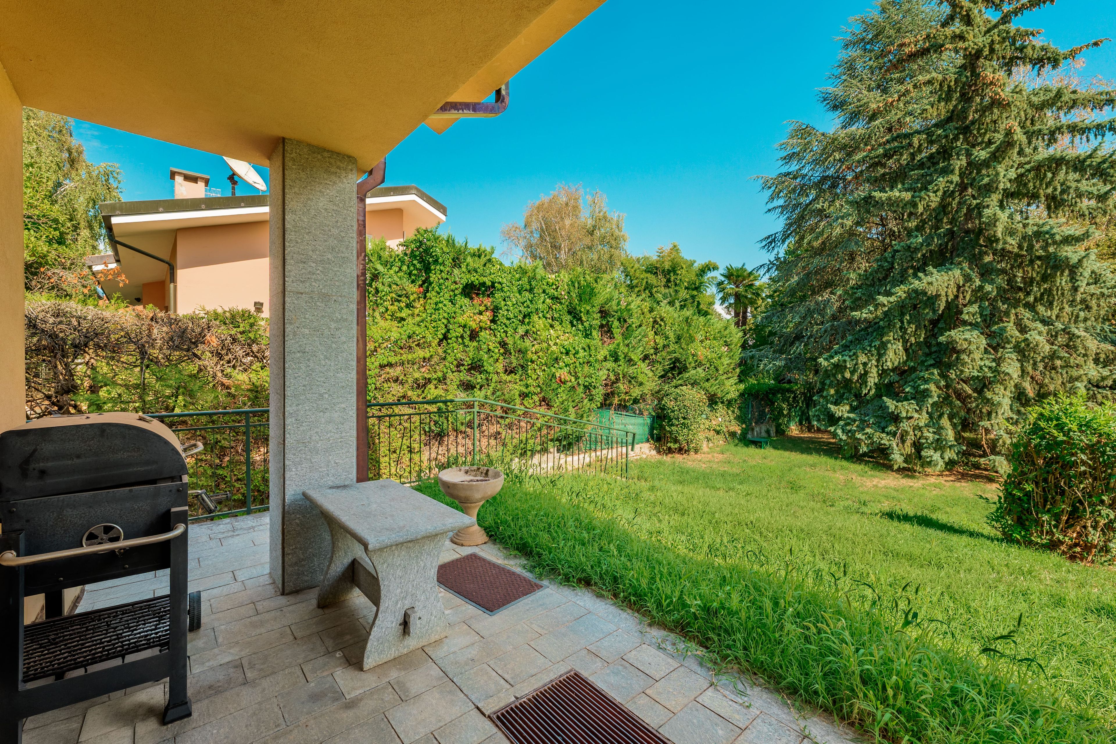 Une terrasse avec un barbecue, des sièges d’extérieur et une vue sur un jardin et des arbres bien entretenus.