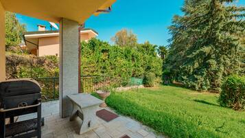 Une terrasse avec un barbecue, des sièges d’extérieur et une vue sur un jardin et des arbres bien entretenus.