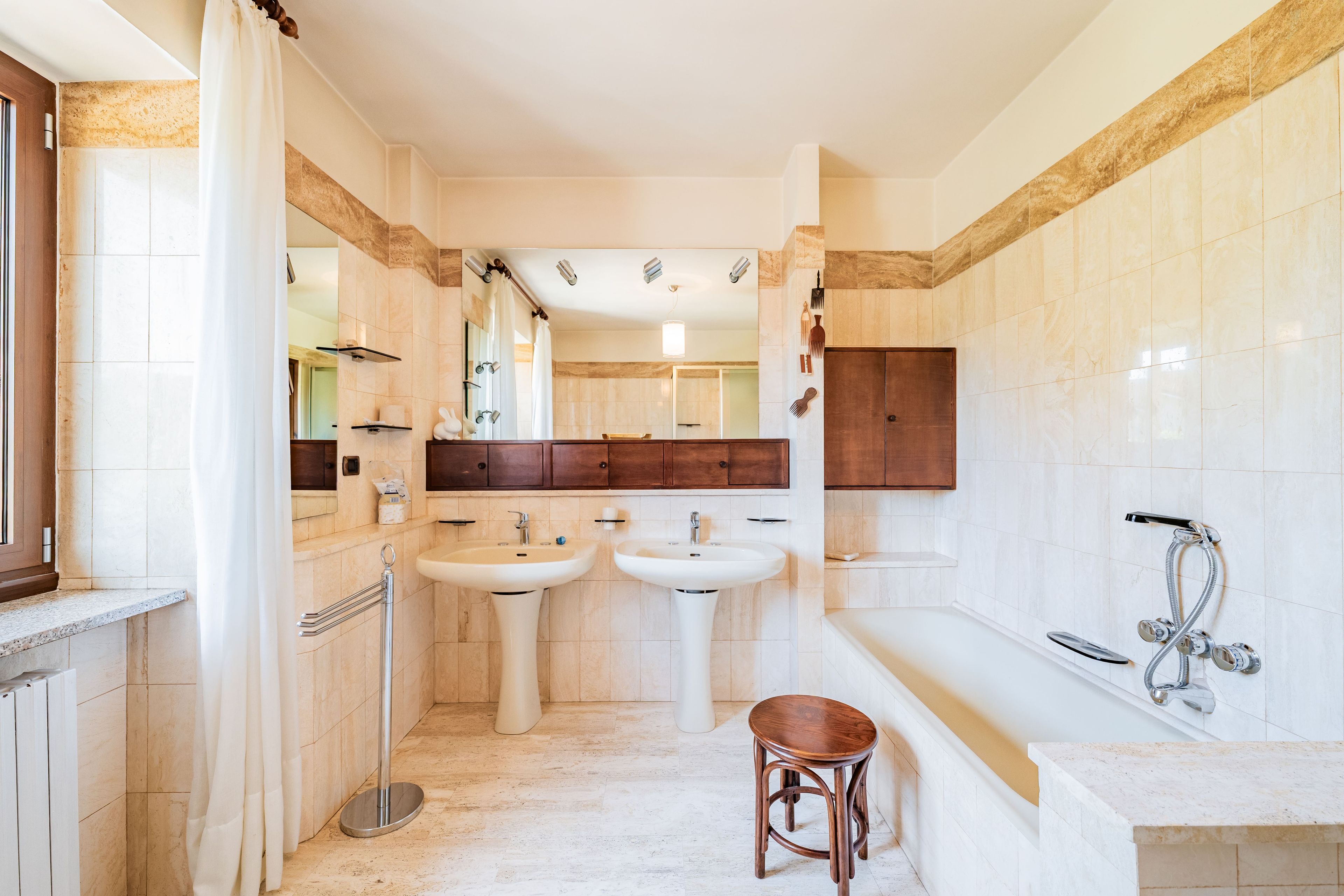 Un baño con dos lavamanos, una bañera, una ducha y un taburete de madera.