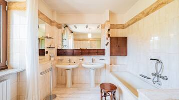 Un baño con dos lavamanos, una bañera, una ducha y un taburete de madera.