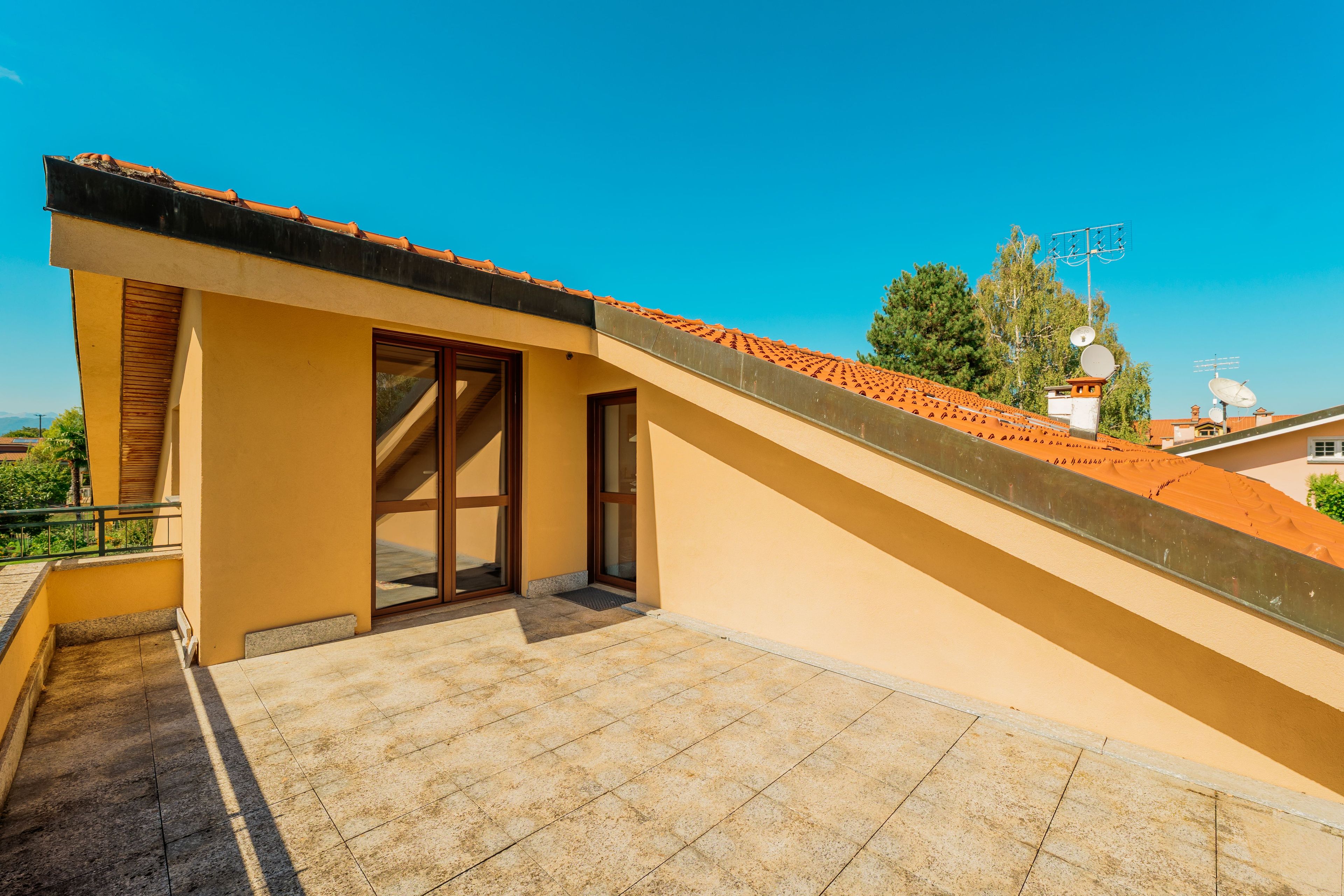 A residential building with a sloped roof, a balcony with a tiled floor, and a clear blue sky in the background.