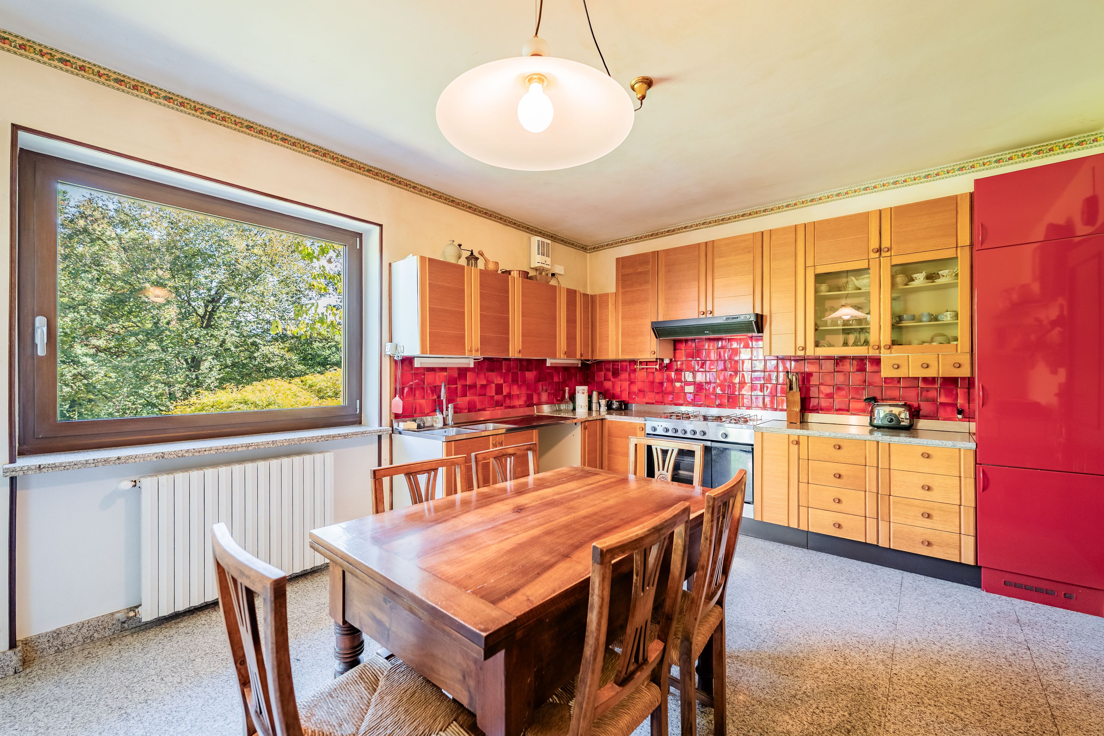 A kitchen with wooden cabinets, a red refrigerator, and a dining table with chairs.