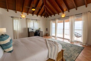 Une chambre avec un grand lit, un bureau et une vue sur la mer par les fenêtres.