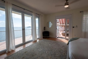 Ein Schlafzimmer mit einer großen Schiebeglastür, die auf einen Balkon mit Meerblick führt.